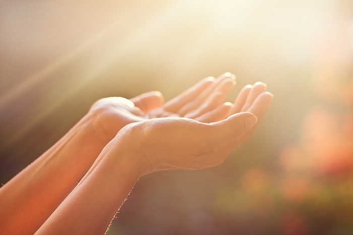 Photo of a person holding both hands up while the sun shines on them. 